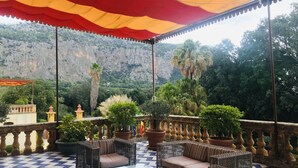 A terrace with wicker furniture, a tiled floor, and a view of a mountainous landscape.