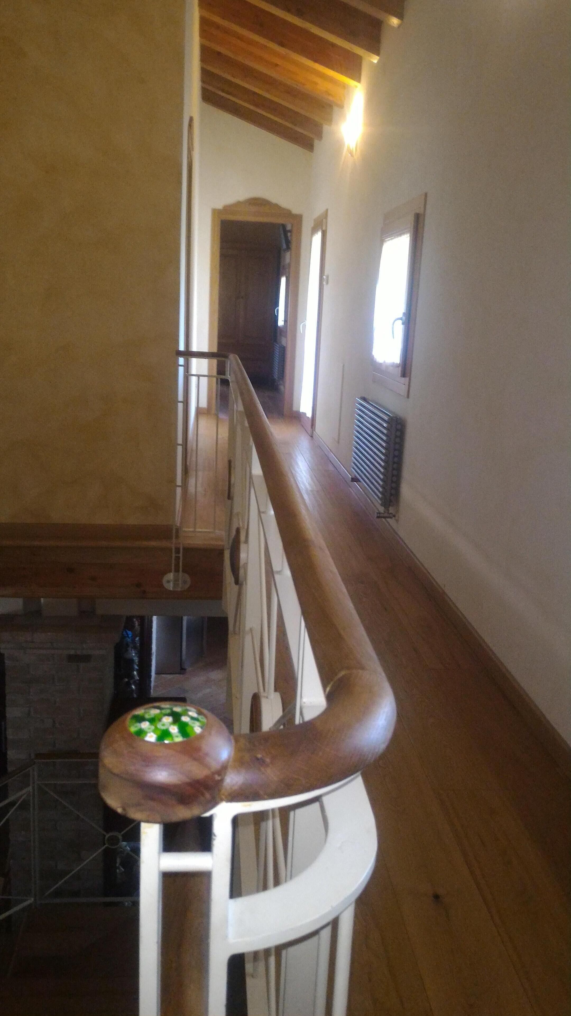 A wooden staircase with a handrail, a radiator on the wall, and a window with a view of the outside.