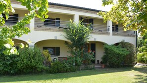 A two-story building with a balcony, surrounded by well-maintained greenery and a lawn.