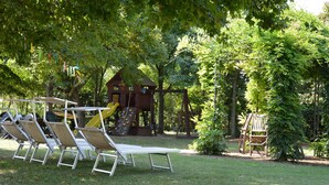 A playground with slides and swings, surrounded by trees and grass.