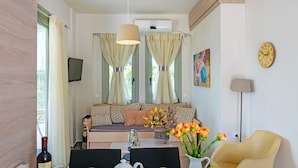 Een gezellige woonkamer met een bank, een eettafel met stoelen, een aan de muur bevestigde televisie en een klok.
