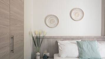 Een moderne slaapkamer met een houten garderobe, een nachtkastje met decoratieve borden, een vaas met bloemen, en een bed met witte en teal kussens.