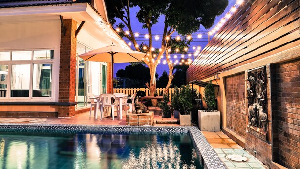 A swimming pool area with a tiled deck, outdoor furniture, and string lights. - Hansa Paradise Hill Pool Villa (Pattaya)