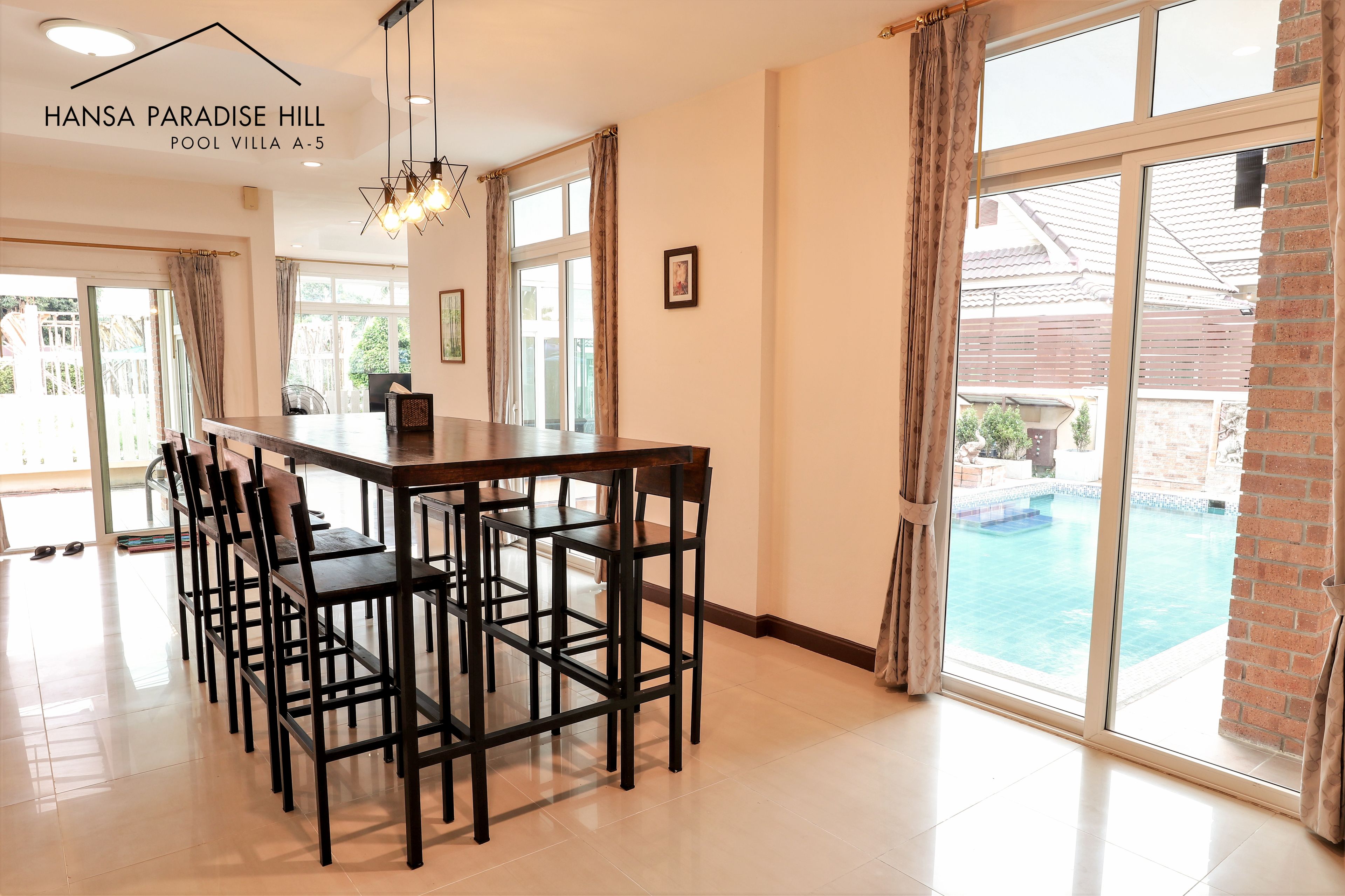 Una cocina moderna con una larga mesa de comedor y sillas, ventanas amplias y vistas a una piscina.