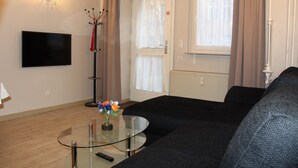 A living room with a black sofa, a glass coffee table, a flat-screen TV, and a vase with flowers.