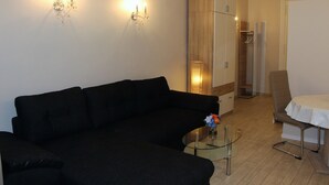 A modern living room with a black sofa, a glass coffee table, and a dining area with a white table and chairs.