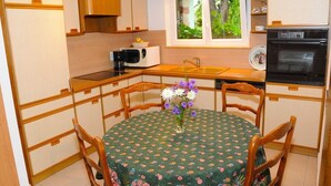 Una cucina compatta con mobili in legno, un forno a microonde, un lavello e un forno. C'è un tavolo da pranzo con sedie e un vaso di fiori.