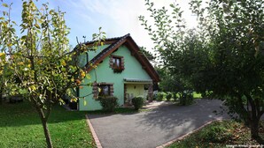 Una casa a due piani con facciata verde, tetto spiovente e un piccolo portico con sedie.