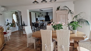 Un coin repas avec une table en bois et des chaises en osier, entouré de plantes en pot et d’une armoire blanche.