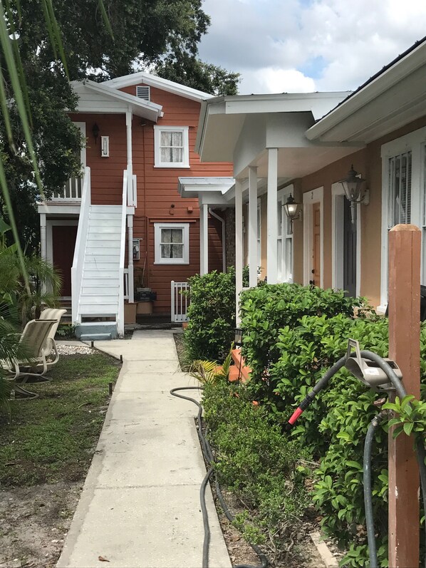 A two-story house with a covered porch, a concrete pathway, and a garden area with bushes and a hose.