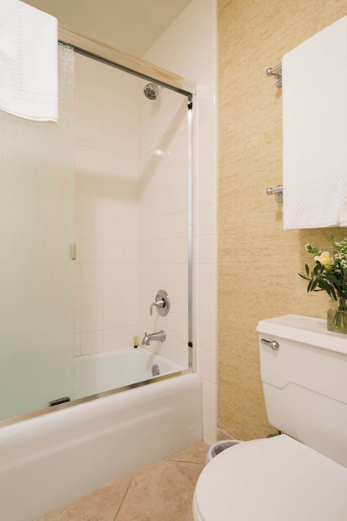 A bathroom with a glass-enclosed shower, a white bathtub, and a toilet.