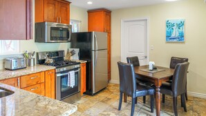 Una cocina con armarios de madera, electrodomésticos de acero inoxidable, una mesa de comedor con sillas y un cuadro en la pared.