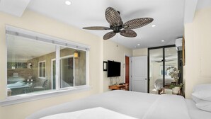 Habitación de hotel moderna con una cama grande, ventilador de techo, televisión y vistas al área exterior.