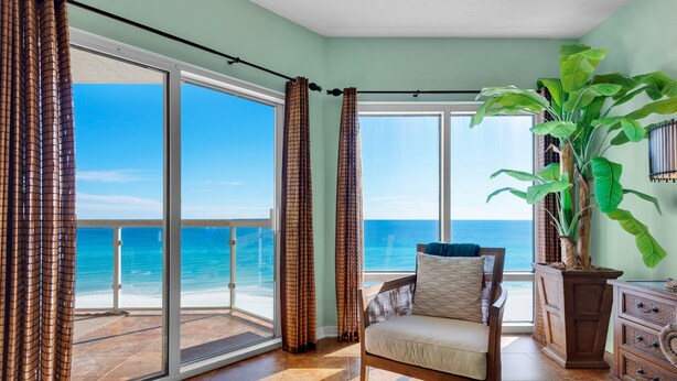 A room with a view of the ocean, a chair, a large plant, and a wooden cabinet. - Gulf Front Condo with Luxury Furnishings and Beach Chairs  (Pensacola Beach)