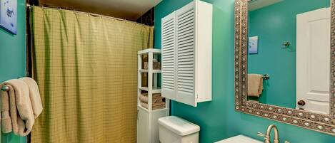 Un baño con pared verde, inodoro blanco, lavamanos con espejo y cortina de ducha.