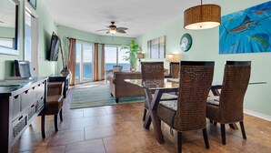 A spacious living room with a dining area, large windows, and a view of the ocean. - Gulf Front Condo with Luxury Furnishings and Beach Chairs  (Pensacola Beach)