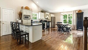 A kitchen with white cabinets, a central island, a dining table with chairs, and a view of greenery through the window. - "On the Rocks"  Bourbon Trail Getaway (Taylorsville)