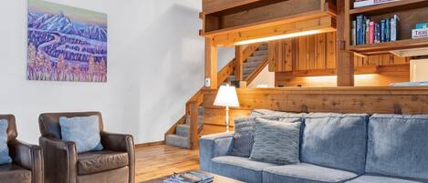 Un salon avec un escalier en bois, un canapé, des fauteuils et une table basse.