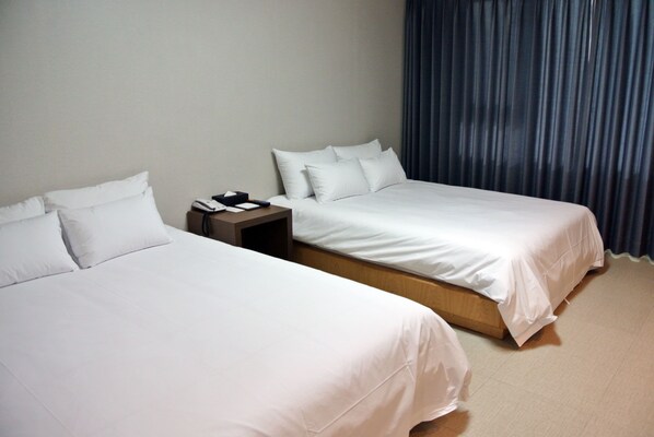 Two single beds with white linens, a wooden nightstand, and a dark curtain. - Jeju Noblesse Tourist Hotel (Jeju City)