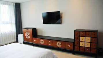 Habitación de hotel con cama, televisor montado en la pared y mueble de madera con cajones.