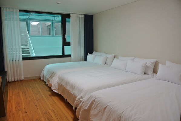 A hotel room with two beds, wooden flooring, a window with curtains, and a view of a building outside. - Jeju Noblesse Tourist Hotel (Jeju City)