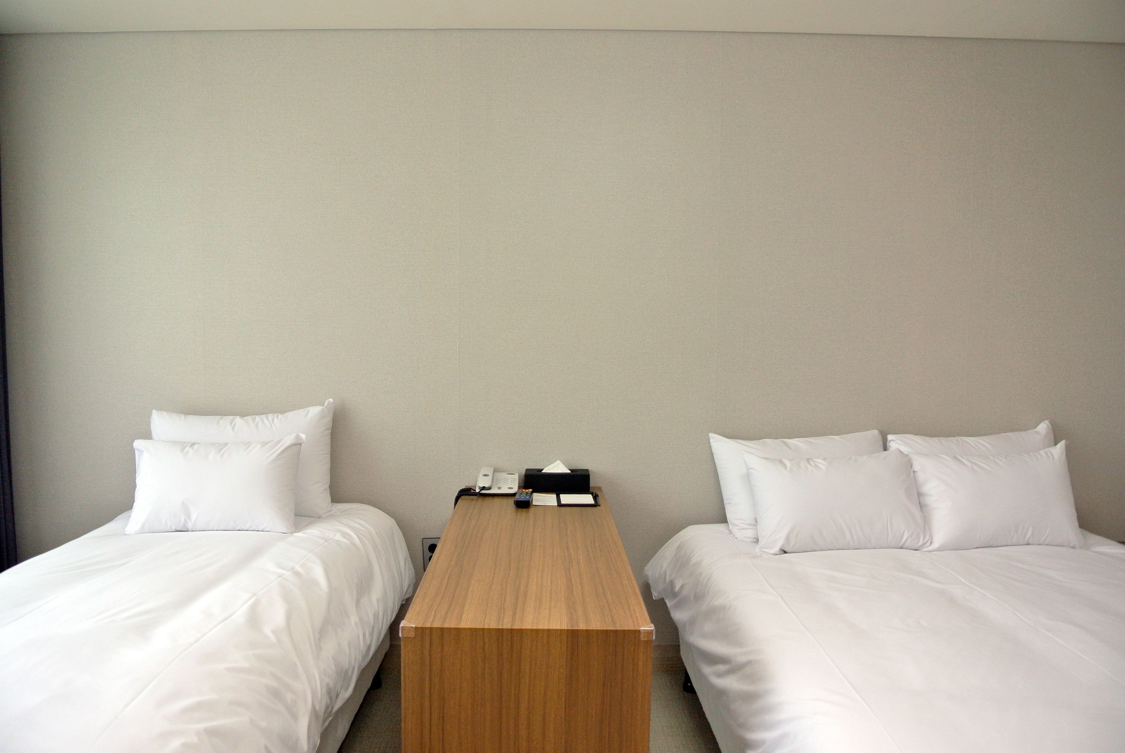 A hotel room with two single beds, a wooden nightstand, and a telephone.