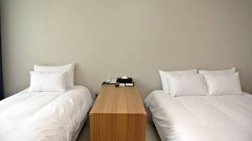 A hotel room with two single beds, a wooden nightstand, and a telephone.