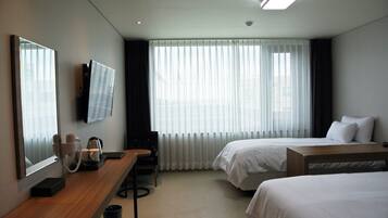 Een hotelkamer met twee bedden, een bureau met koffiezetapparaat, een televisie en grote ramen met gordijnen.