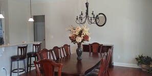 A dining area with a large wooden table, six chairs, a vase of flowers, a chandelier, and a mirror on the wall.