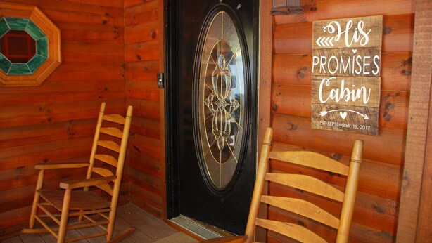 A wooden cabin interior with a black door, two wooden rocking chairs, and a sign on the wall that reads "His Promises Cabin EST. September 16, 2017". - Two bedroom cabin, King Beds, WI-FI, hot tub, pool, views (Pigeon Forge)