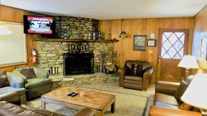 A cozy living room with a stone fireplace, leather sofas, a coffee table, and a television mounted on the wall.