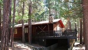 A rustic cabin with a stone foundation, wooden deck, and a chimney.