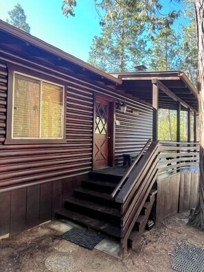 Puuinen mökki, jossa on kuisti, portaikko ja ikkunallinen ovi.