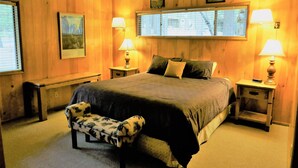 A bedroom with a large bed, two bedside tables with lamps, a bench, and a chair.