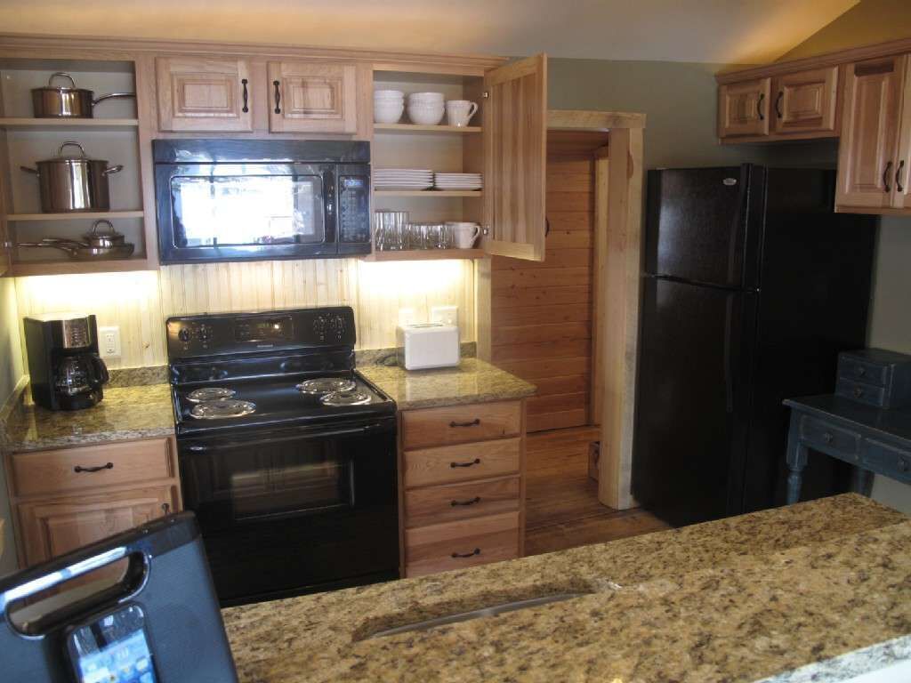 A kitchen with wooden cabinets, a black stove, a microwave, and a refrigerator.