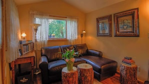 A cozy living room with a leather sofa, a bookshelf, a lamp, and two framed pictures on the wall.