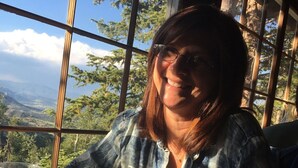 A person sitting at a table with a glass of water and a smartphone, with a view of trees and mountains through large windows.