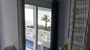 Una habitación con vista al mar, una silla de mimbre, una mesa blanca y una silla blanca.