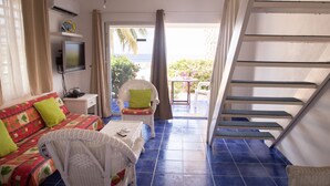 Una habitación con cama, una silla, una mesa, un televisor y una escalera que lleva a un balcón con vistas al mar.