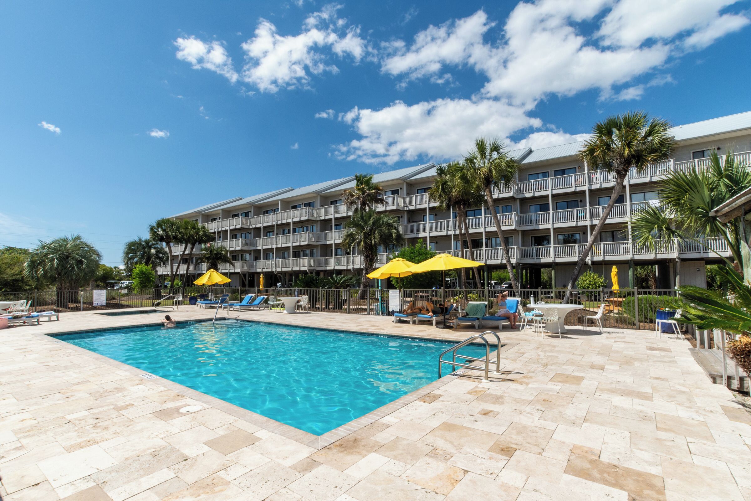 A hotel with a swimming pool, outdoor seating, and palm trees.