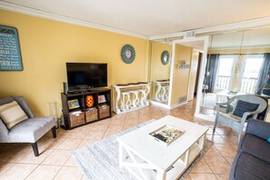 A living room with a TV, white furniture, and a yellow wall. - Views for miles Pinnacle Port Heated pool Check this out May & Summer (PANAMA CITY BEACH)