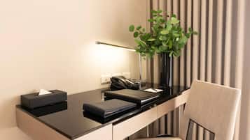 Un moderno mostrador de hotel con superficie negra, un florero con hojas verdes, un teléfono negro y una silla color beige.