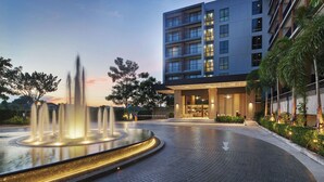 A modern hotel entrance with a water feature in front, a well-lit lobby, and a multi-story building with balconies. - The Park Nine Hotel Suvarnabhumi  (Bangkok)