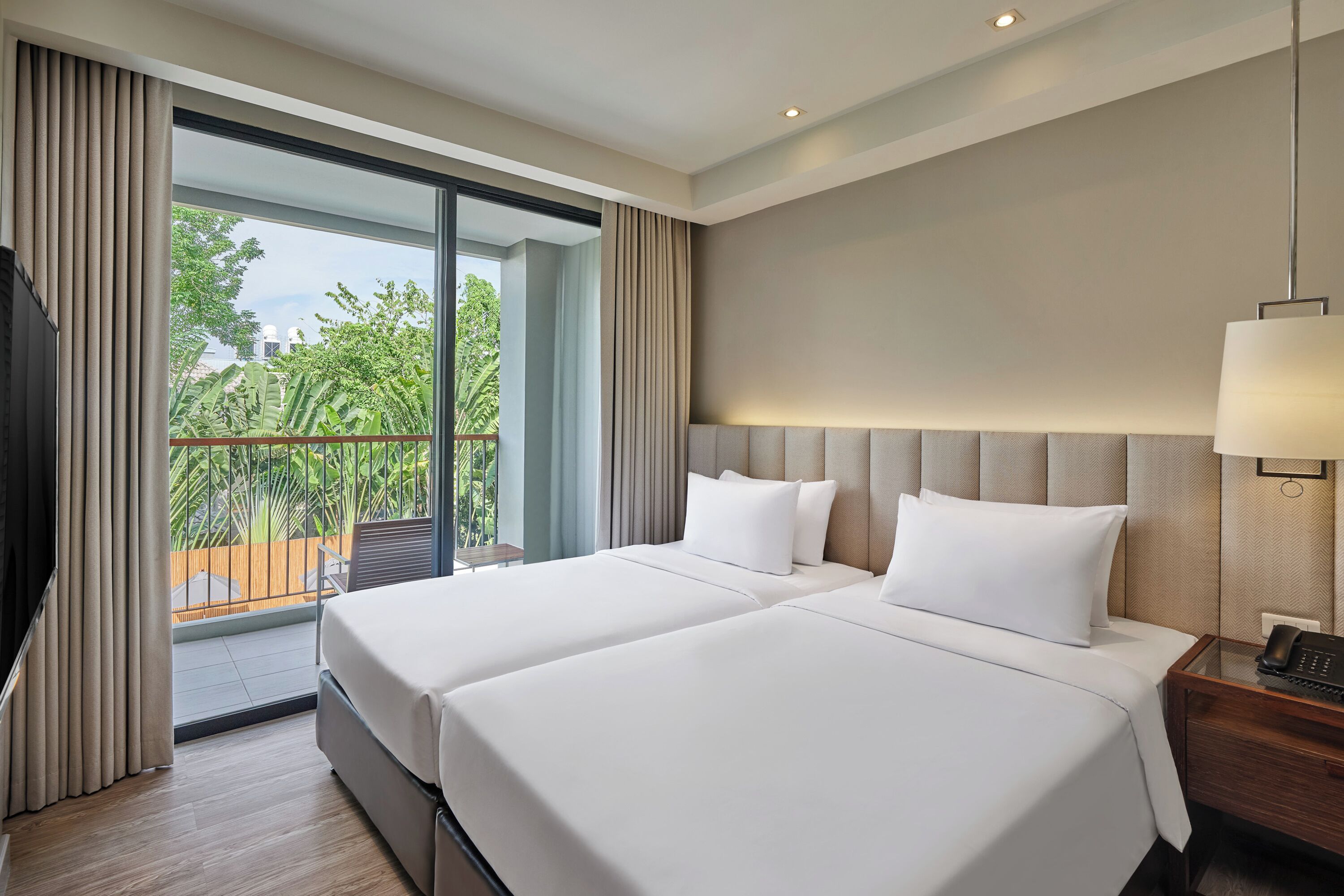 A hotel room with two beds, a large window, and a view of greenery.