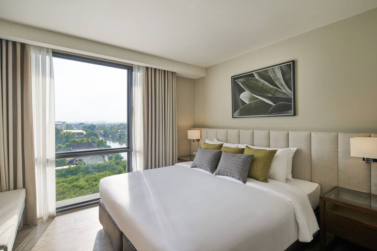 Ein Hotelzimmer mit einem großen Bett, Blick auf einen Fluss und eine Skyline, und einem modernen Design.