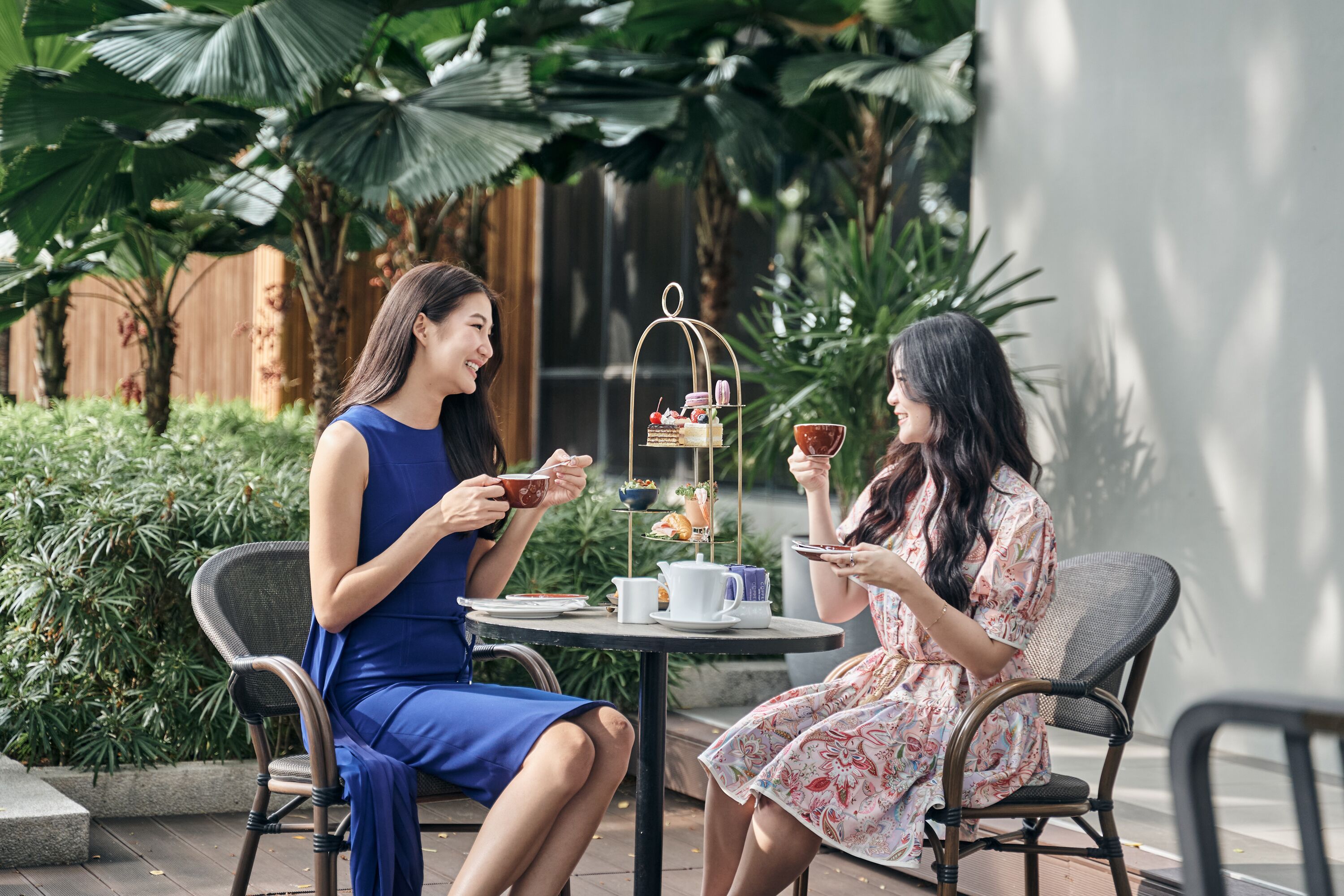 Dos mujeres sentadas en una mesa al aire libre con un servicio de té, rodeadas de abundante vegetación.