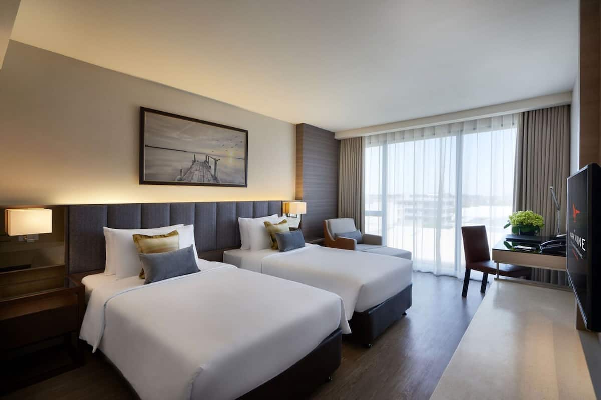 Ein Hotelzimmer mit zwei Betten, einem Schreibtisch, einem Stuhl, einem Fernseher und einem großen Fenster mit Vorhängen.