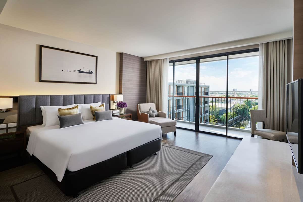 Ein modernes Hotelzimmer mit einem großen Bett, einem Schreibtisch, einem Sessel und einem Fernseher. Das Zimmer verfügt über einen Balkon mit Blick auf die Stadt.
