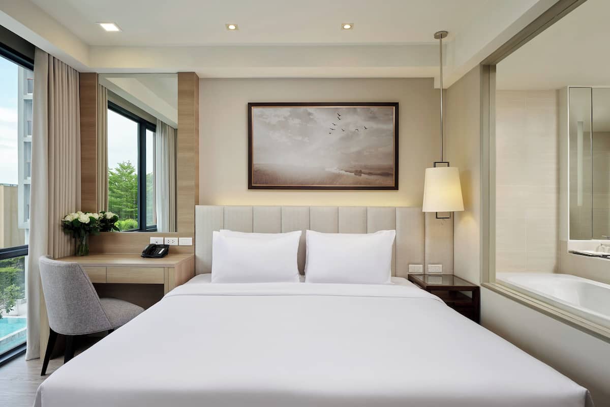 Ein Hotelzimmer mit einem großen Bett, einem Schreibtisch, einem Stuhl, einem Gemälde, einer Lampe und einem Badezimmer mit einer Badewanne.