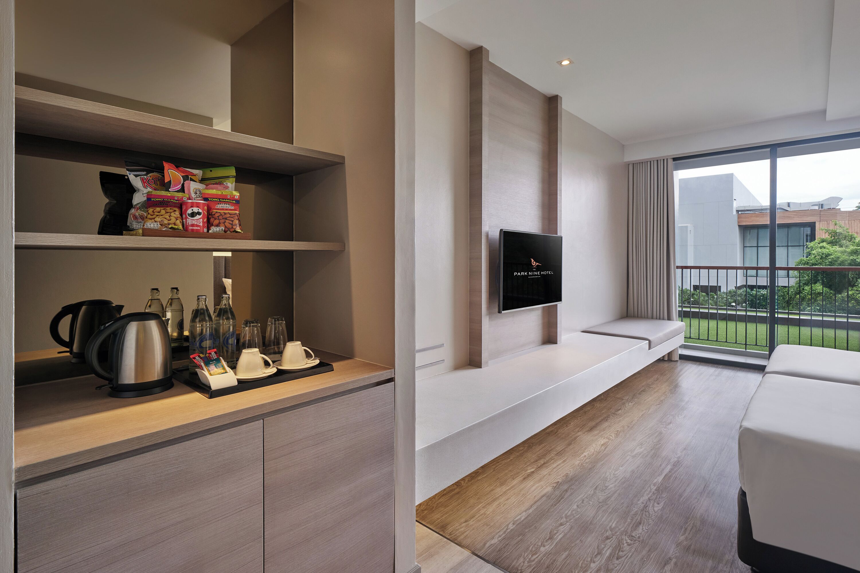 Une chambre d’hôtel moderne dotée d’une kitchenette, d’un téléviseur à écran plat fixé au mur, d’un coin salon avec un banc et d’un balcon offrant une vue sur la ville.